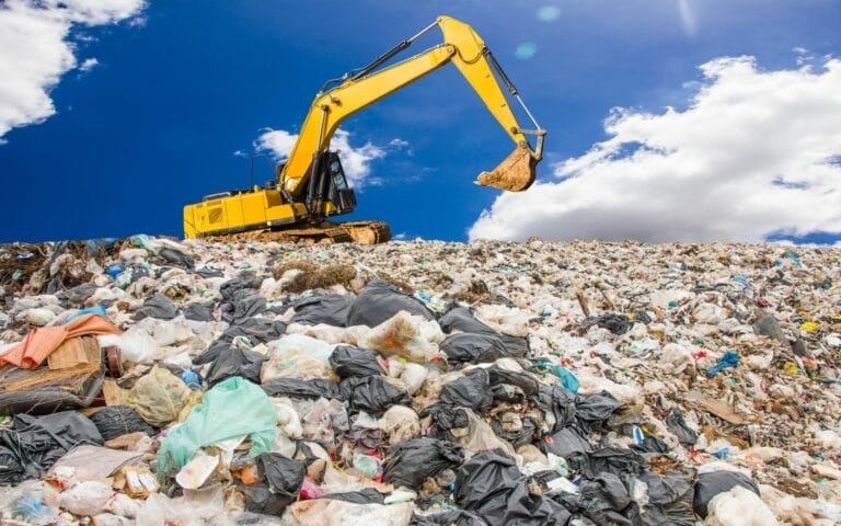 Excavator working in large landfill, blue sky background.