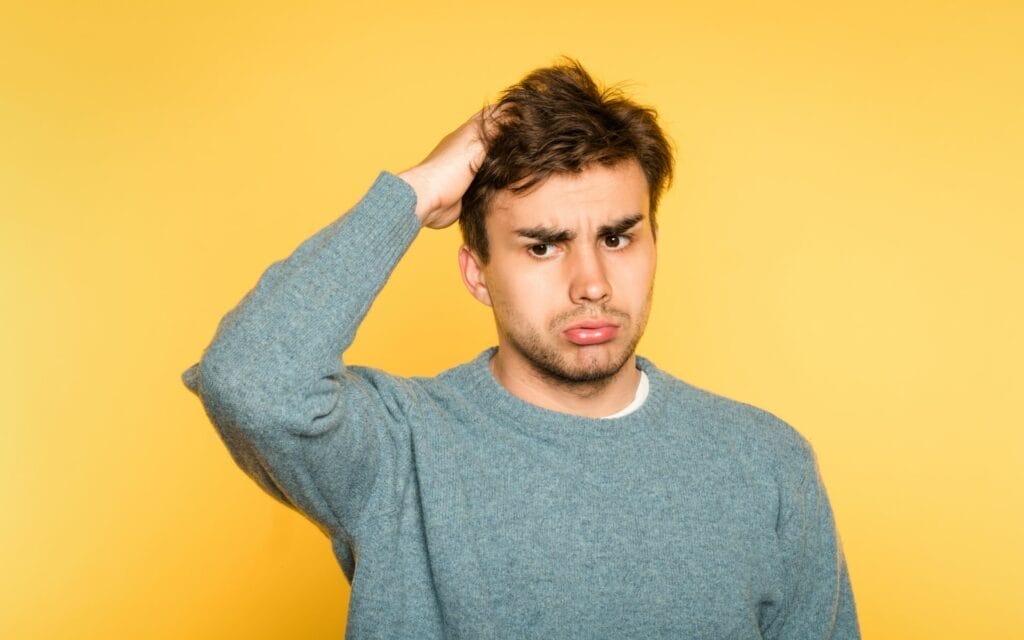 Confused man scratching head, yellow background.