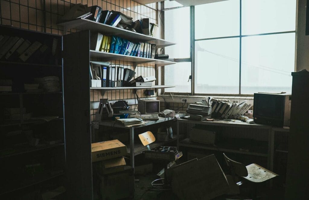 Cluttered office with shelves of binders, old equipment.
