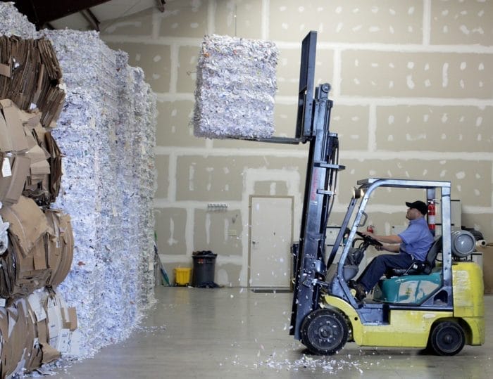 Forklift moving stacked cardboard bales in warehouse