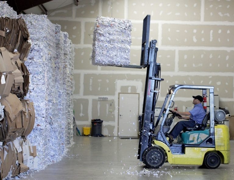 Forklift moving stacked cardboard bales in warehouse
