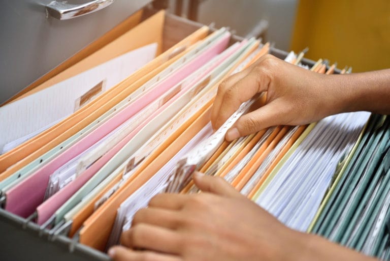 Hands organizing files in a cabinet drawer.