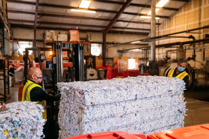 Workers with shredded paper bales in recycling facility.