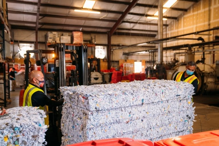 Workers with shredded paper bales in recycling facility.