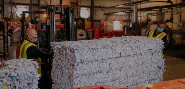 Workers managing shredded paper bales in recycling plant.