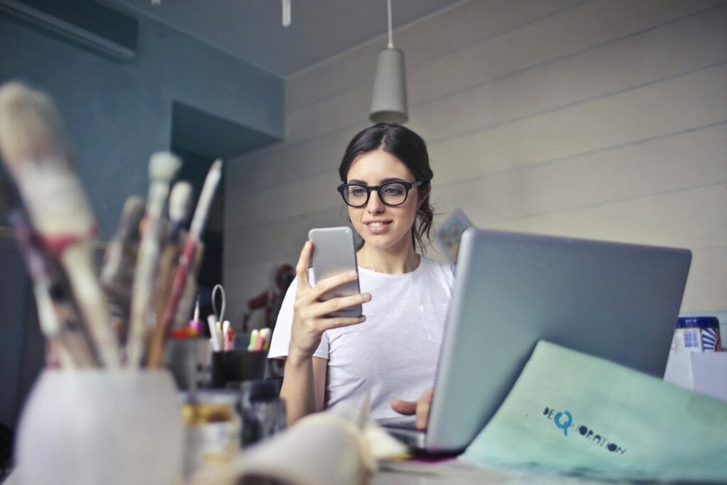 Woman using phone and laptop at a desk.