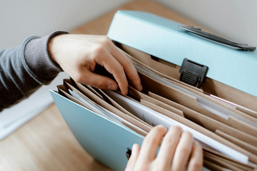 Hands sorting documents in blue accordion folder.