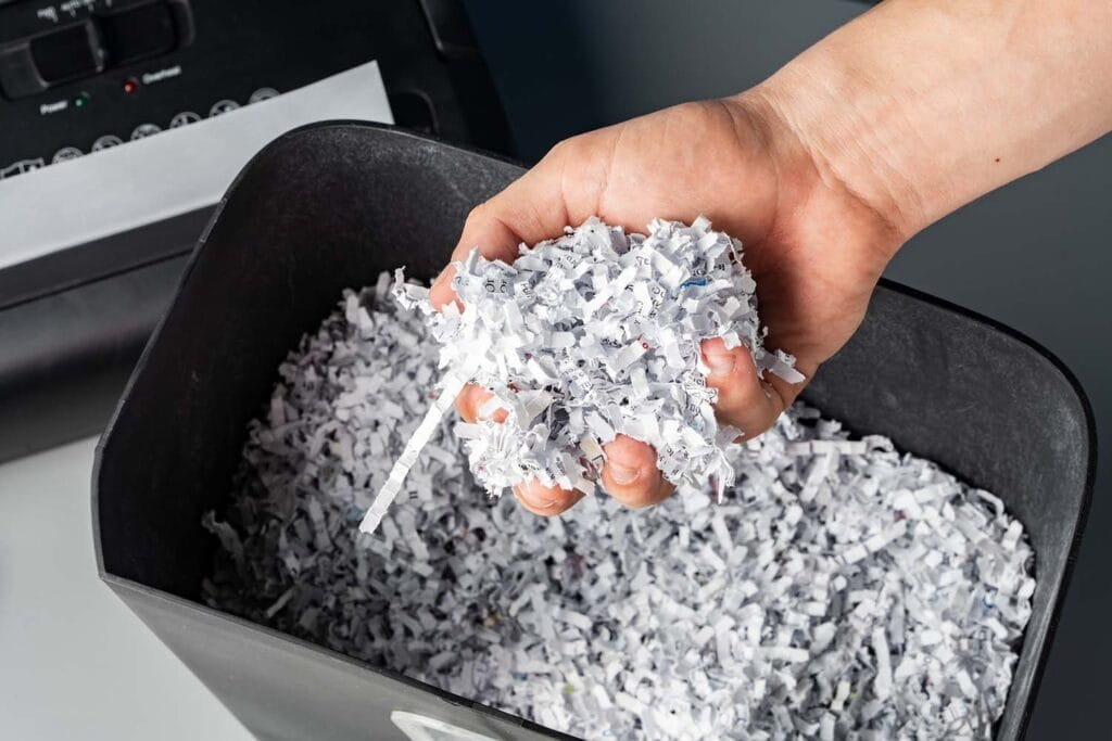 Hand holding shredded paper pieces above bin.