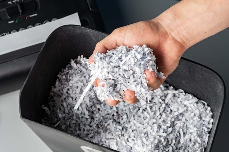 Hand holding shredded paper pieces above bin.