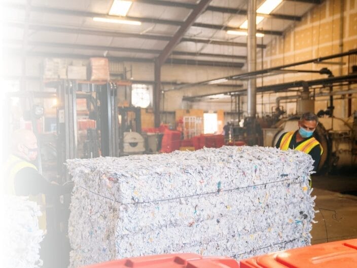 Workers handling bales of recycled paper after secure shredding in texas